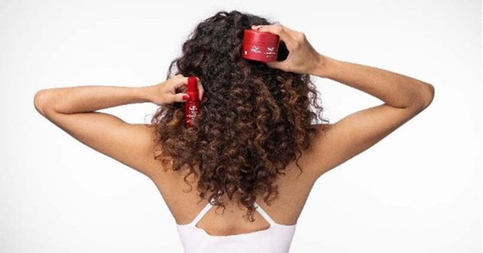 Mulher de costas com cabelo encaracolado segura produtos Wella Ultimate Repair para o cuidado do cabelo danificado pelo verão
