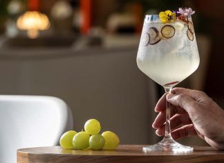 Evolution Bar Fest agita o Estoril entre cocktails e novas tendências da mixologia Mão segura um copo de cocktail decorado com flores e rodelas de fruta, numa imagem associada ao EVOLUTION Bar Fest