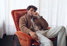 Moda masculina com linhas urbanas e cortes descontraídos na nova coleção da OOTO Moda masculina OOTO com blusão castanho, malha clara e calças em tom cru, num homem sentado numa poltrona laranja
