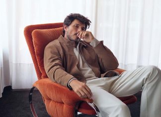 Moda masculina com linhas urbanas e cortes descontraídos na nova coleção da OOTO Moda masculina OOTO com blusão castanho, malha clara e calças em tom cru, num homem sentado numa poltrona laranja