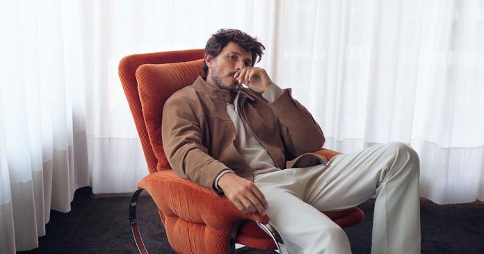 Moda masculina OOTO com blusão castanho, malha clara e calças em tom cru, num homem sentado numa poltrona laranja