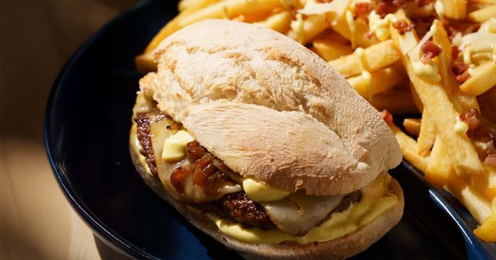 Prego de Hambúrguer da Portugália servido em pão com queijo, cebolada e molho, acompanhado por batatas fritas