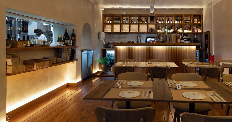 Interior da sala de refei&ccedil;&otilde;es do restaurante Vizinhos do Rei em Odivelas com mesas dispostas e balc&atilde;o iluminado ao fundo