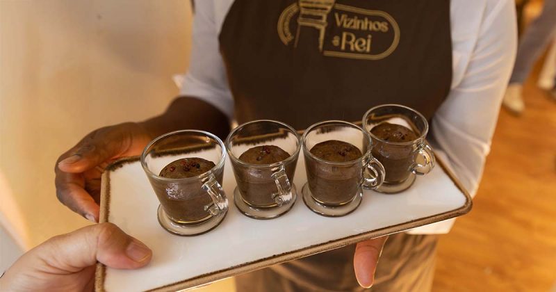 Empregado com avental oficial do restaurante Vizinhos do Rei em Odivelas a segurar uma travessa com ch&aacute;venas de mousse de chocolate com pimenta rosa