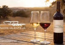 Vinhos alentejanos ligam compras a experiências no Alentejo Vinhos alentejanos com garrafa e copos de vinho numa paisagem do Alentejo