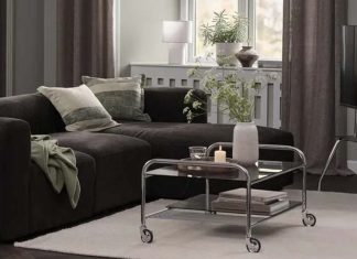 Decoração de outono da JYSK conjuga o brilho dos cromados com o conforto dos tons castanhos Sala com sofá escuro, mesa de centro em vidro e cromado com rodas e suporte de televisão na decoração de outono da JYSK
