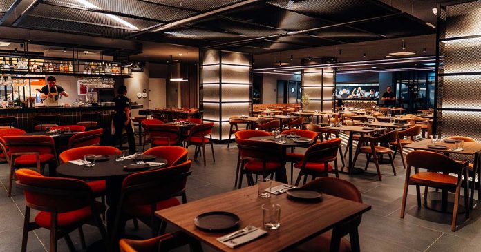 Sala com mesas de madeira, cadeiras em tons quentes e bar ao fundo, onde são servidos os grelhados no 550º, em Lisboa