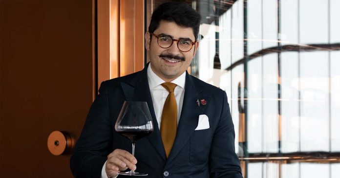 Marc Pinto, representante de Portugal na eleição do melhor sommelier do mundo, segura um copo de vinho tinto e um prato no restaurante.