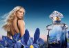Perfume personalizado com a fragrância de sempre e um frasco diferente Modelo e frasco de L’Heure Bleue da Guerlain entre íris azuis, em imagem que acompanha a iniciativa de perfume personalizado