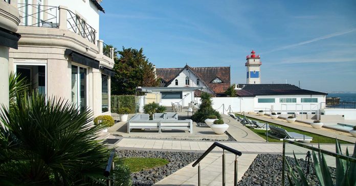 Restaurantes do Farol Hotel junto ao Atlântico em Cascais Terraço junto aos restaurantes do Farol Hotel, com espreguiçadeiras, vista para o mar e um farol ao fundo