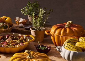 Tachos e panelas Le Creuset levam as formas e as cores do outono à mesa Tachos e panelas Le Creuset em forma de abóbora, em laranja, amarelo e branco, sobre uma mesa com legumes e ervas aromáticas