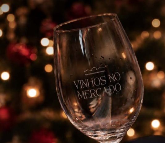 Vinhos no Mercado junta mais de 30 produtores no Porto entre provas e arte Copo Vinhos no Mercado com decoração natalícia ao fundo, no ambiente do evento.